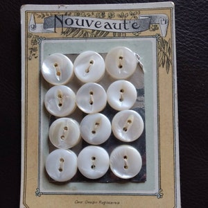 May include: A card of twelve white mother-of-pearl buttons with two holes each. The card is labeled "Nouveauté" and "Card Design Registered".