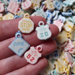 May include: Assortment of colorful plastic charms shaped like road signs. The charms feature text such as "Through Stop Traffic", "Ill US 20", "Curve", and "Ind US 52".