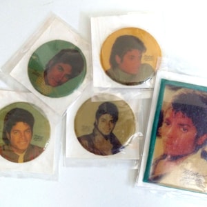 May include: Five round stickers featuring a portrait of Michael Jackson. The stickers are in various colors, including green, yellow, and brown. The stickers are packaged in clear plastic.