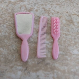 May include: A set of three pink plastic hair care tools: a hand mirror, a comb, and a brush.