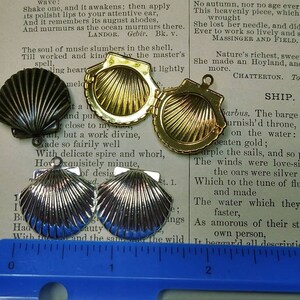 May include: An assortment of seashell-shaped pendants in various metallic finishes: silver, gold, and dark bronze. The pendants are displayed on a vintage book page, showcasing their intricate details and textures. The pendants have a loop for attaching to a chain.