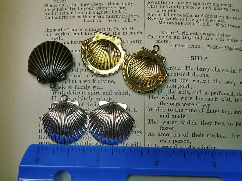 May include: An assortment of seashell-shaped pendants in various metallic finishes: silver, gold, and dark bronze. The pendants are displayed on a vintage book page, showcasing their intricate details and textures. The pendants have a loop for attaching to a chain.