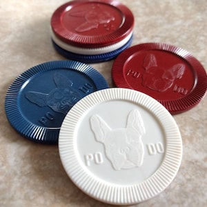 May include: Four poker chips with a dog design. Two chips are red, one is blue, and one is white. The chips have the text "PO  DO" on them.