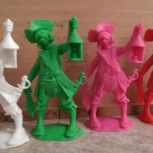May include: Four plastic pirate figurines, each holding a lantern. The pirates are wearing different colored clothing: white, green, pink, and red.