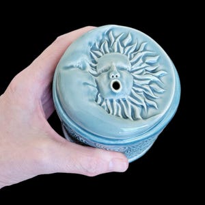 May include: A blue ceramic incense burner with a sun and moon design. The sun has a face and a hole in its mouth for incense to be burned.