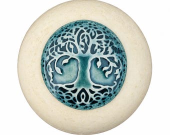 May include: A round ceramic knob with a cream-colored outer edge and a central circular inlay featuring a teal and dark blue tree of life design with intricate branches and roots set against a glossy, textured background finish.