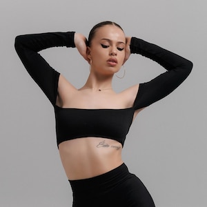 May include: A black two-piece outfit comprising a crop top with long sleeves and wide-leg trousers. The crop top has a square neckline and the trousers have side slits. The outfit is made of a soft, flowing fabric.