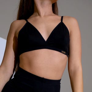 Peut inclure: Un soutien-gorge noir à fines bretelles et un legging taille haute assorti. Le soutien-gorge a un design encolure en V. La tenue est faite d'une matière douce et extensible. La personne porte une montre noire au poignet gauche.