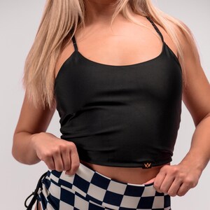 May include: Black crop top with spaghetti straps and high-waisted shorts. The shorts feature a navy and white checkered pattern and drawstring ties on the sides. The top has a small gold logo.