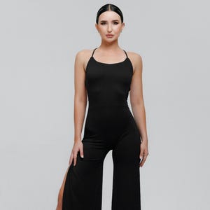 May include: A black jumpsuit with a halter neckline and wide-leg pants. The jumpsuit features a high slit on one leg and is paired with black heeled boots. The outfit is designed for a sleek, modern look.