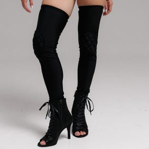 Könnte beinhalten: Schwarze High-Waist-Hose mit Kordelzugdetails und passenden Oberschenkel-Leggings mit gesteppten Knieschonern. Das Model trägt schwarze, offene Stiefeletten mit Absatz. Das Outfit ist ganz schwarz.