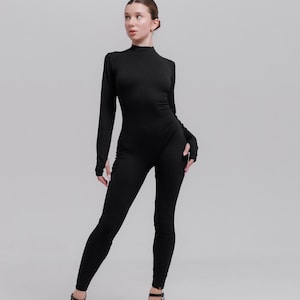 May include: A woman wearing a black long-sleeved jumpsuit with a mock neck and high-heeled platform sandals.