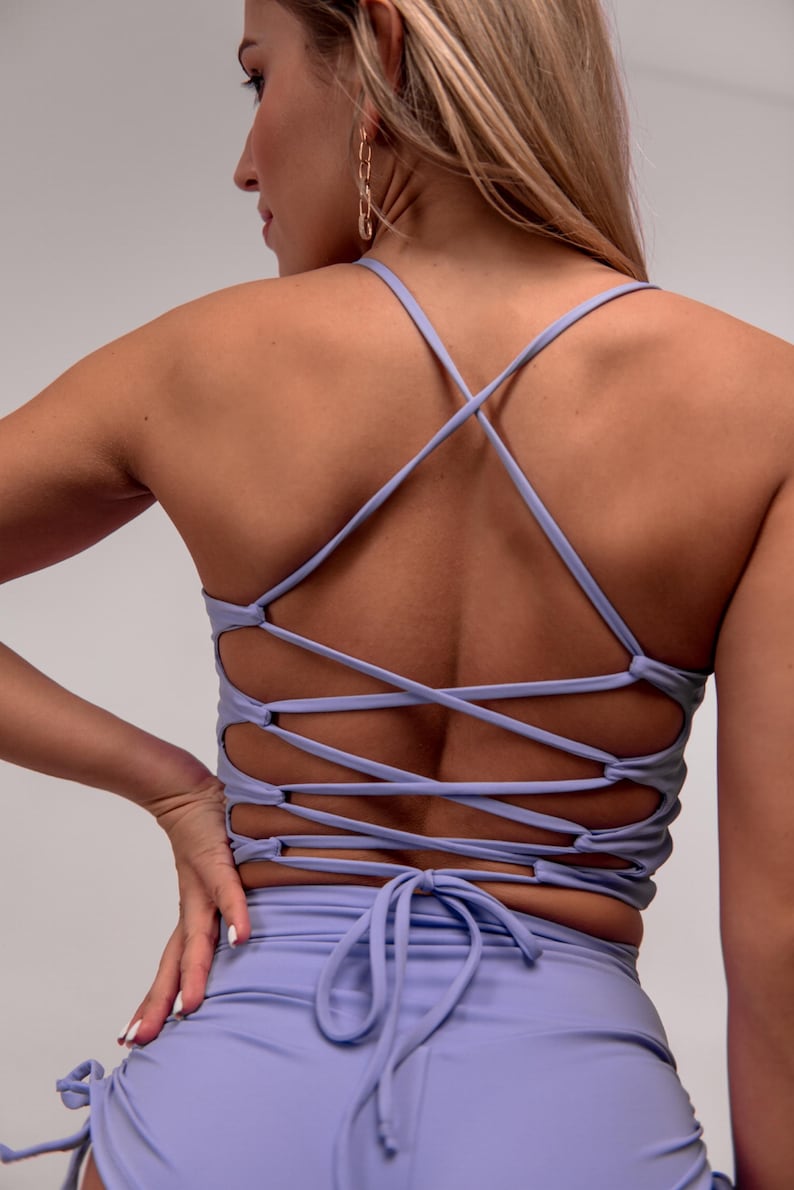 May include: A light purple sports bra with crisscross straps on the back. The bra is paired with matching shorts. The back of the bra has a lace-up design. The shorts have a drawstring tie.