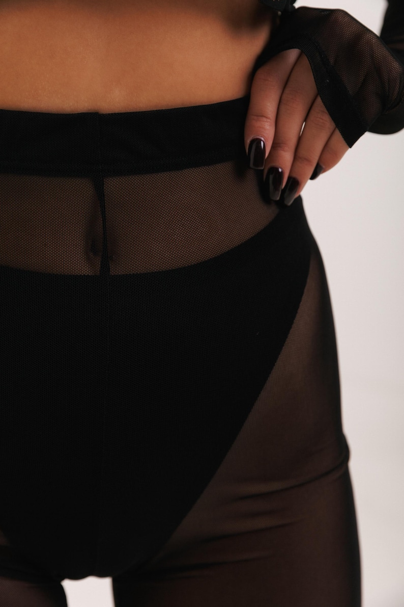 May include: Black mesh leggings with a high waist and a wide waistband. The leggings are sheer and have a black lining.