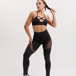 Op de afbeelding: Zwarte sportset met een sport-bh met een uniek uitgesneden ontwerp en een legging met hoge taille en mesh panelen. De outfit wordt gecombineerd met turquoise en zwarte sportschoenen. De algehele look is strak en modern, perfect voor workouts.