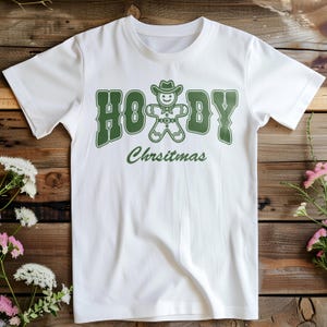 May include: White t-shirt with a green graphic of a gingerbread man wearing a cowboy hat and the text "Howdy Christmas".
