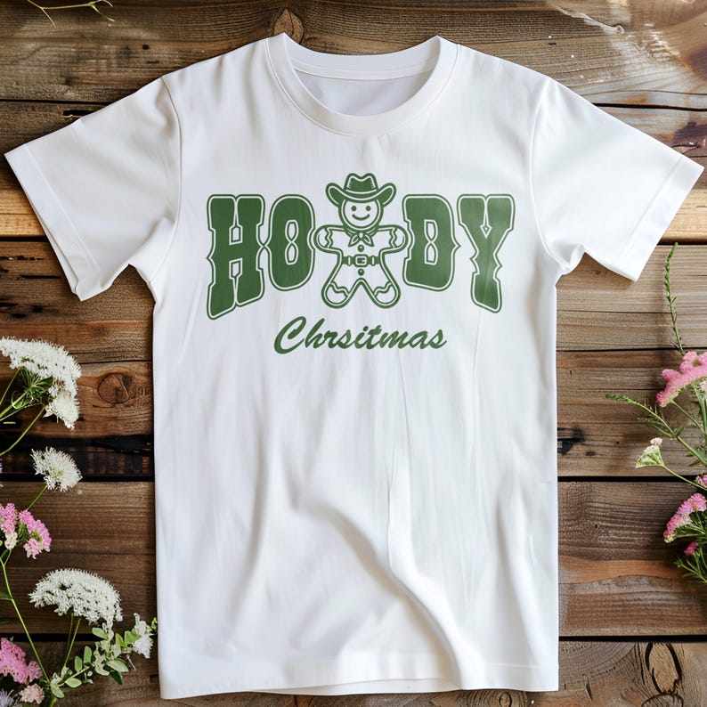 May include: White t-shirt with a green graphic of a gingerbread man wearing a cowboy hat and the text "Howdy Christmas".
