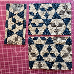 May include: Three rectangular quilted fabric pieces featuring a geometric pattern of dark blue, cream, and brown diamonds and triangles. The fabric has a visible stitched texture and is arranged on a pink cutting mat with inch markings.