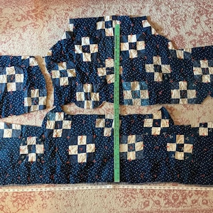 May include: A dark blue fabric with a white and red floral pattern featuring white square block patches. A green ruler is placed vertically, measuring approximately 24 inches, and a white measuring tape shows a length of 58 inches.
