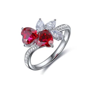 May include: A silver ring featuring a floral design with heart-shaped red gemstones and clear accent stones. The band curves gracefully, embellished with small, sparkling stones, creating an elegant and eye-catching piece of jewelry.