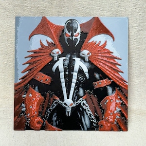 May include: Square artwork featuring the Spawn comic book character. The figure is depicted in black, white, and red, with a detailed design. The artwork has a textured appearance and is set against a light gray background.
