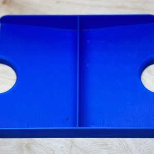 May include: A blue plastic tray with two compartments, each with a semi-circular cutout on one side.