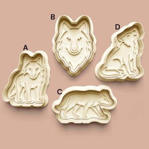 Puede incluir: Cuatro cortadores de galletas de plástico beige con forma de lobos. Las formas incluyen un lobo de pie, una cabeza de lobo, un lobo caminando y un lobo aullando. Los cortadores están etiquetados A, B, C y D.