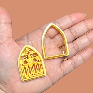 Puede incluir: Dos cortadores de galletas de plástico amarillo con forma de ventanas arqueadas. Un cortador tiene un diseño detallado con una cruz y arcos más pequeños. El otro cortador es una forma de arco simple.