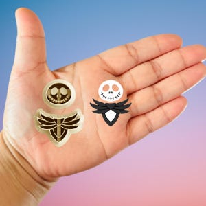 Puede incluir: Tres cortadores de galletas con el tema de Jack Skellington. Uno es un diseño circular con una cara sonriente, otro es una pajarita estilizada y el tercero es un diseño circular con una cara sonriente.