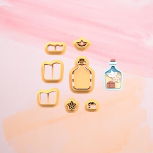Könnte beinhalten: Ein Set mit neun goldenen Ausstechern, darunter eine Flasche, ein Boot, ein Stern, eine Truhe und drei verschiedene Buchformen.