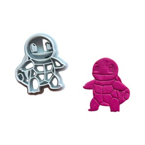Puede incluir: Dos cortadores de galletas de plástico con forma de tortuga. El cortador de la izquierda es azul claro y el de la derecha es rosa.