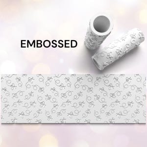 May include: White embossed rolling pins with a bee design, alongside a matching embossed paper strip. The word "EMBOSSED" is printed in black. The rolling pins are cylindrical and feature a repeating pattern of bees and dotted flight paths.