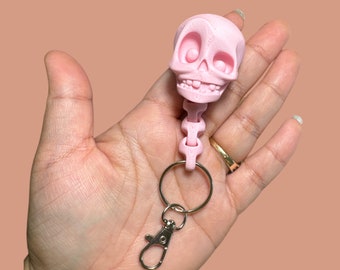 May include: A pink plastic skeleton keychain with a skull head and a silver chain. The keychain has a silver clasp.