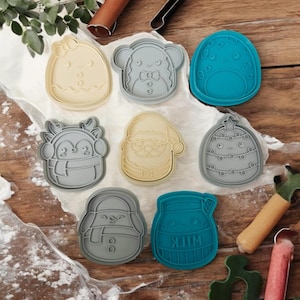May include: Set of eight Christmas cookie cutters in various shapes, including a penguin, snowman, Santa Claus, gingerbread person, milk carton, and a Christmas tree. The cutters are made of plastic and are in various shades of blue and gray.