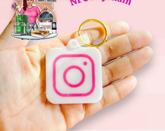 May include: White square NFC keychain with a pink Instagram logo. The keychain has a gold-colored ring and a clear plastic attachment. The text "NFC Keychain" is in pink. The background is a gradient of pink.