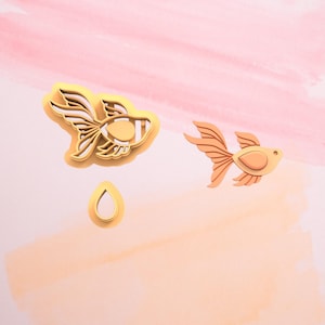 May include: A set of three cookie cutters in the shape of goldfish and a water drop. The cutters are made of gold-colored metal.