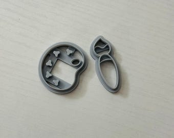 May include: Two gray plastic cookie cutters, one shaped like a paintbrush and the other shaped like a paint palette.