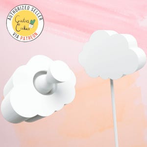 May include: Two white cloud-shaped cake toppers. One cloud has a small white cylinder in the center. The other cloud is on a white stick.