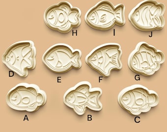May include: Ten different cookie cutters shaped like fish. The cutters are made of white plastic and have a variety of designs, including a clownfish, a pufferfish, and a swordfish.