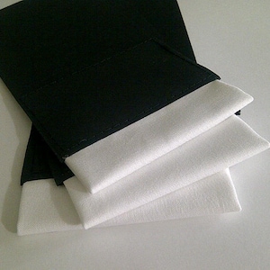 May include: Three black fabric wrist cuffs with white fabric lining. The cuffs are folded on top of each other.