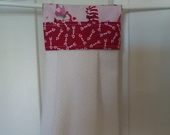 Pode incluir: Toalha de cozinha branca com uma parte superior estampada em vermelho e branco. A parte superior apresenta um tecido vermelho com setas brancas e um tecido com personagens temáticos do Dia dos Namorados. A parte inferior da toalha tem duas listras vermelhas.