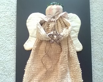May include: A handmade angel figurine with a white crocheted dress, a green wreath on its head, and a star in its hand. The angel is framed against a black background.