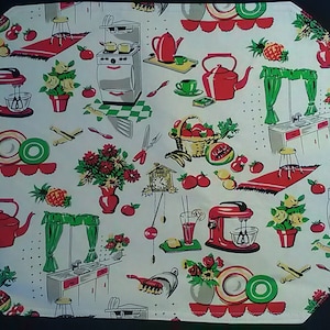 May include: A white kitchen-themed placemat with a repeating pattern of red kitchen appliances, red and green fruits and vegetables, and red and green floral arrangements. The placemat has a scalloped edge.