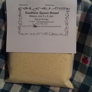 May include: A white bag with a label that reads "Southern Spoon Bread Makes one 8 x 8 dish Apron Strings E-Mail: JPShags@gmail.com (757) 718-1253 www.ETSY.comshop/ApronStringsHandmade". The bag contains a yellow powder.