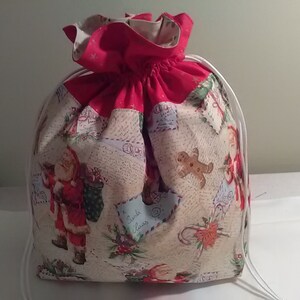 May include: A red and white Christmas gift bag with a drawstring closure. The bag is decorated with a Santa Claus, gingerbread man, and other Christmas-themed illustrations. The bag is made of fabric and has a white drawstring.