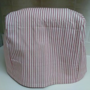 May include: A white and red striped fabric cover for a kitchen appliance. The cover has a rounded shape and is made of a soft, cotton-like material.