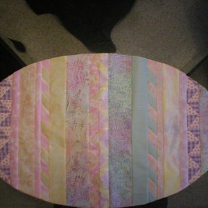 以下が含まれることがあります： ピンクと黄色の楕円形のテーブルランナーで、パッチワークのデザインが施されています。ランナーは、ストライプ、水玉模様、花柄など、さまざまなパターンを持つさまざまな生地で作られています。