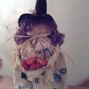 May include: A witch doll with a black hat and a patchwork quilt dress holding a basket of small pumpkins.
