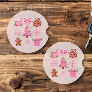 May include: Two car coasters with a Christmas theme. Each coaster features a pink background with illustrations of a gingerbread house, Christmas tree, snowflakes, and a gingerbread man. A car key is in the background.