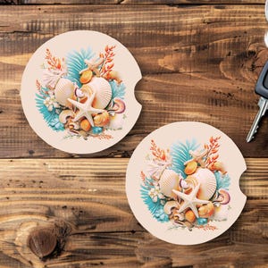 May include: Two round beige coasters with a seashell and starfish design. The coasters feature a blue, green, and orange color scheme with a white background.